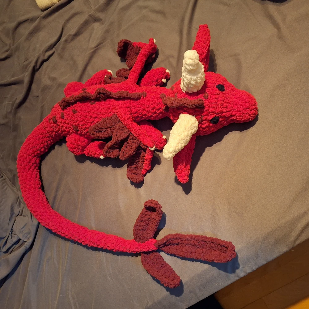 Crocheted baby dragon sitting upright with embroidered details